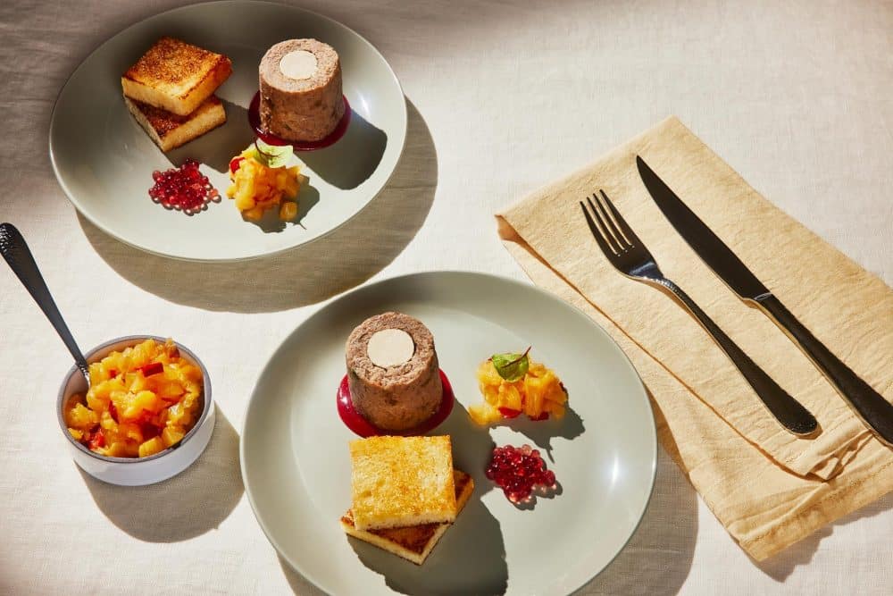 Deux plats réalisés par Maestro Culinaire à base de canard dans une assiette gris, sur une nappe beige, avec des couverts sur une serviette jaune claire.