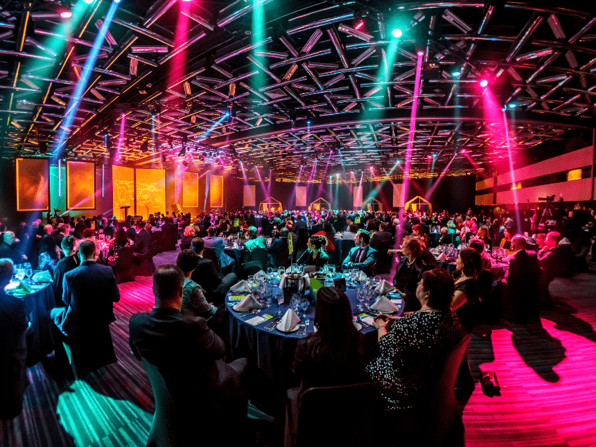 Gala hall with blue and red lights, and people seated at tables.