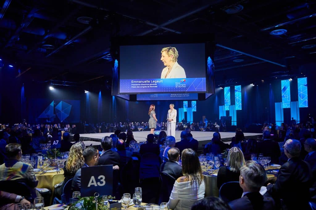 Gala evening with two people on stage and an audience seated at tables around them.