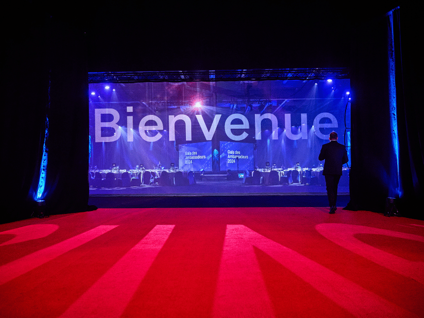 Red carpet with a giant blue screen displaying the word "Welcome," and a person standing on the right, facing away.