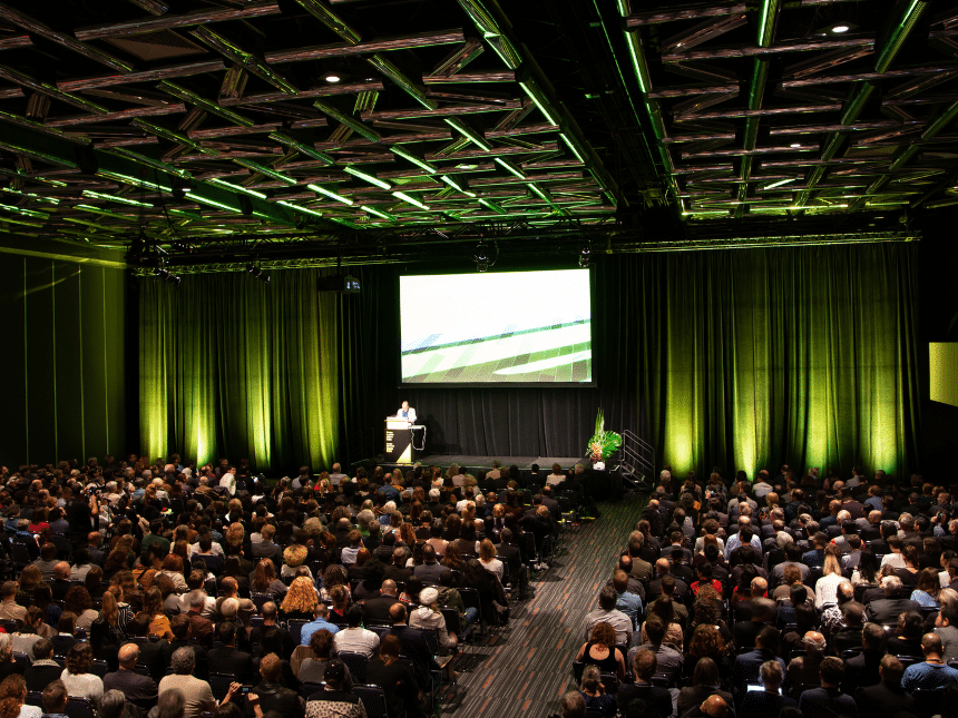 Salle de congrès avec plusieurs participants assis de dos sur des chaises, lumière d'ambiance verte.