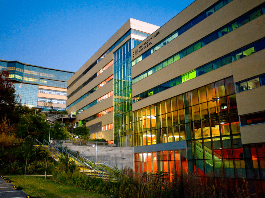 Photo extérieur de Polytechnique Montréal, bâtiment beige avec des fenêtres vertes et rouges, de l'herbe au sol et un ciel bleu.