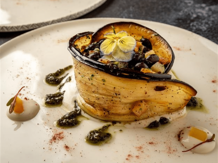Un plat avec des légumes, des fleurs et de l'aubergine sur une assiette de couleur crème.